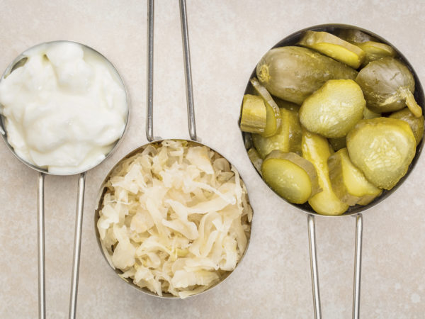 sauerkraut, cucumber pickles and yogurt - popular probiotic fermented food - three measuring cups against ceramic tile