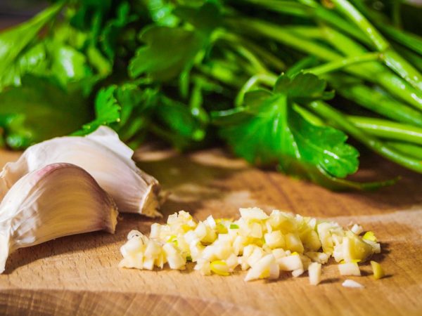 Finely chopped garlic and fresh green leaves of parsley on a wooden kitchen board close up.