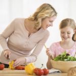 Happy little girl assisting mother in preparing food at kitchen counter