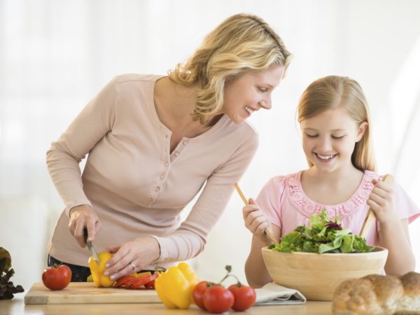 Happy little girl assisting mother in preparing food at kitchen counter
