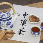 Astragalus herb tea also used in chinese herbal medicine, with cups and calligraphy script on rice paper over bamboo. Translation reads as chinese herbal tea.
