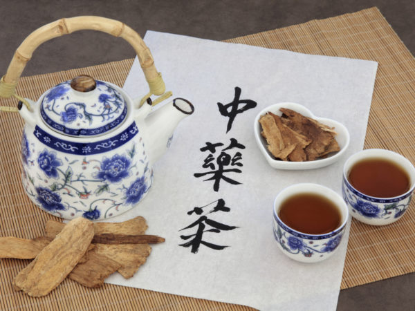 Astragalus herb tea also used in chinese herbal medicine, with cups and calligraphy script on rice paper over bamboo. Translation reads as chinese herbal tea.
