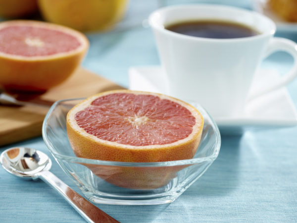 Ruby red grapefruit in a glass bowl with coffee, cutting board and knife in background.  Color corrected, exported 16 bit depth, retouched and saved for maximum image quality.