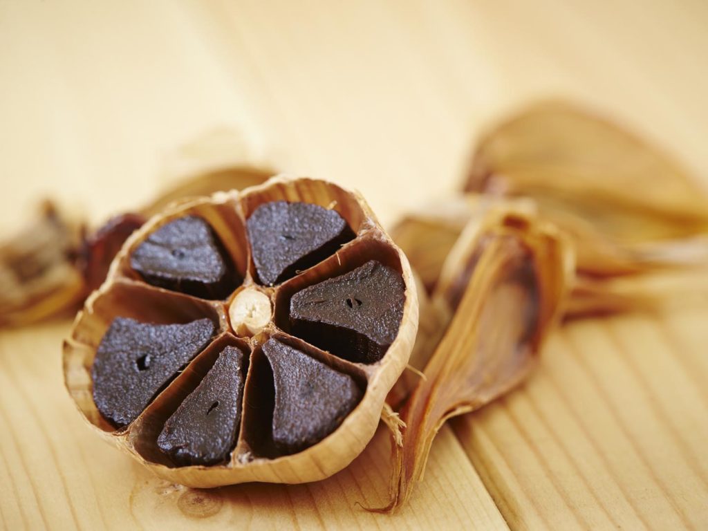 Black garlic on dish, wooden background