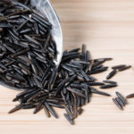 A scoop and a small pile of wild rice on a wooden surface.