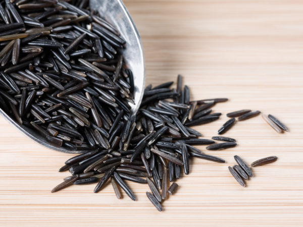 A scoop and a small pile of wild rice on a wooden surface.