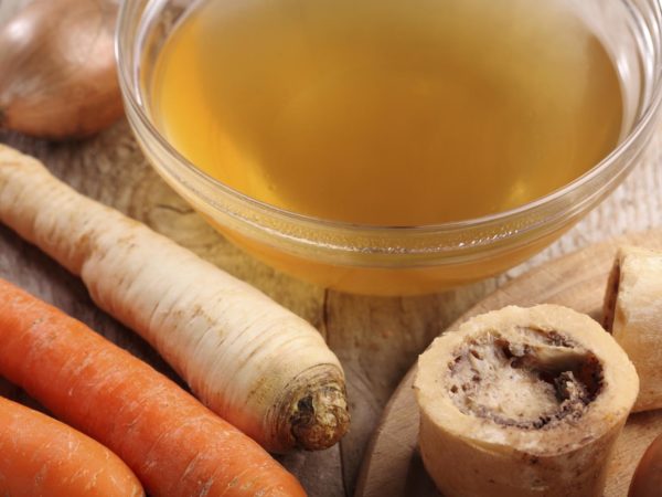 Bowl with beef broth, boiled bones and fresh vegetables.