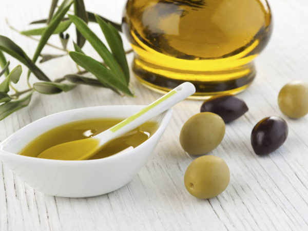 Olive oil and green and black olives on white wooden background