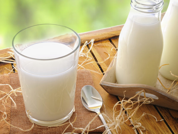 Glass of milk on a table on the field with two bottles of milk