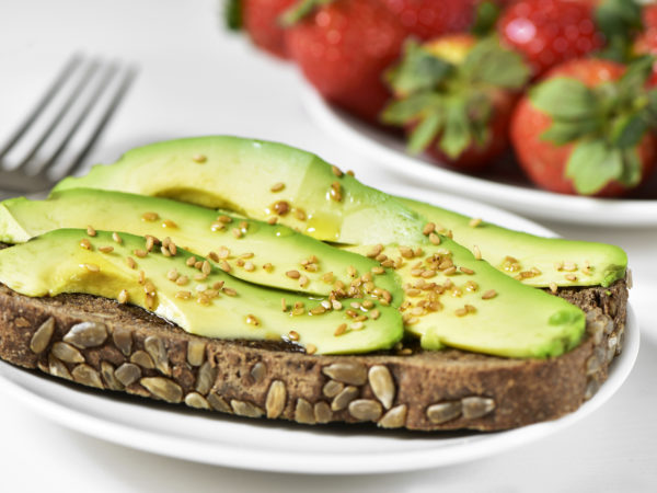 closeup of an avocado toast made with rye bread and a bowl full of strawberries in the background