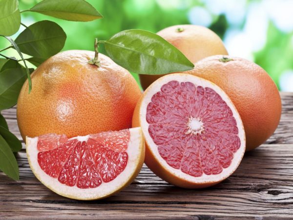 Grapefruits on a wooden table with green foliage on the background.