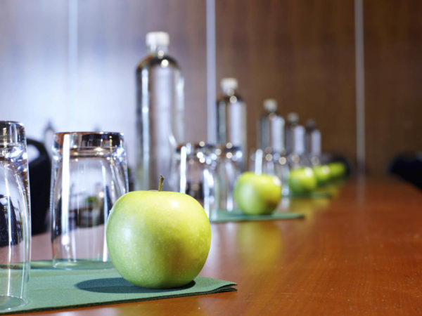 Row of water bottles glasses and apples laid out in preparation for a business conference