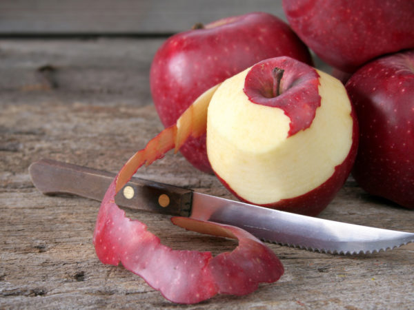 Peeling an apple with a knife on a rustic wood background.