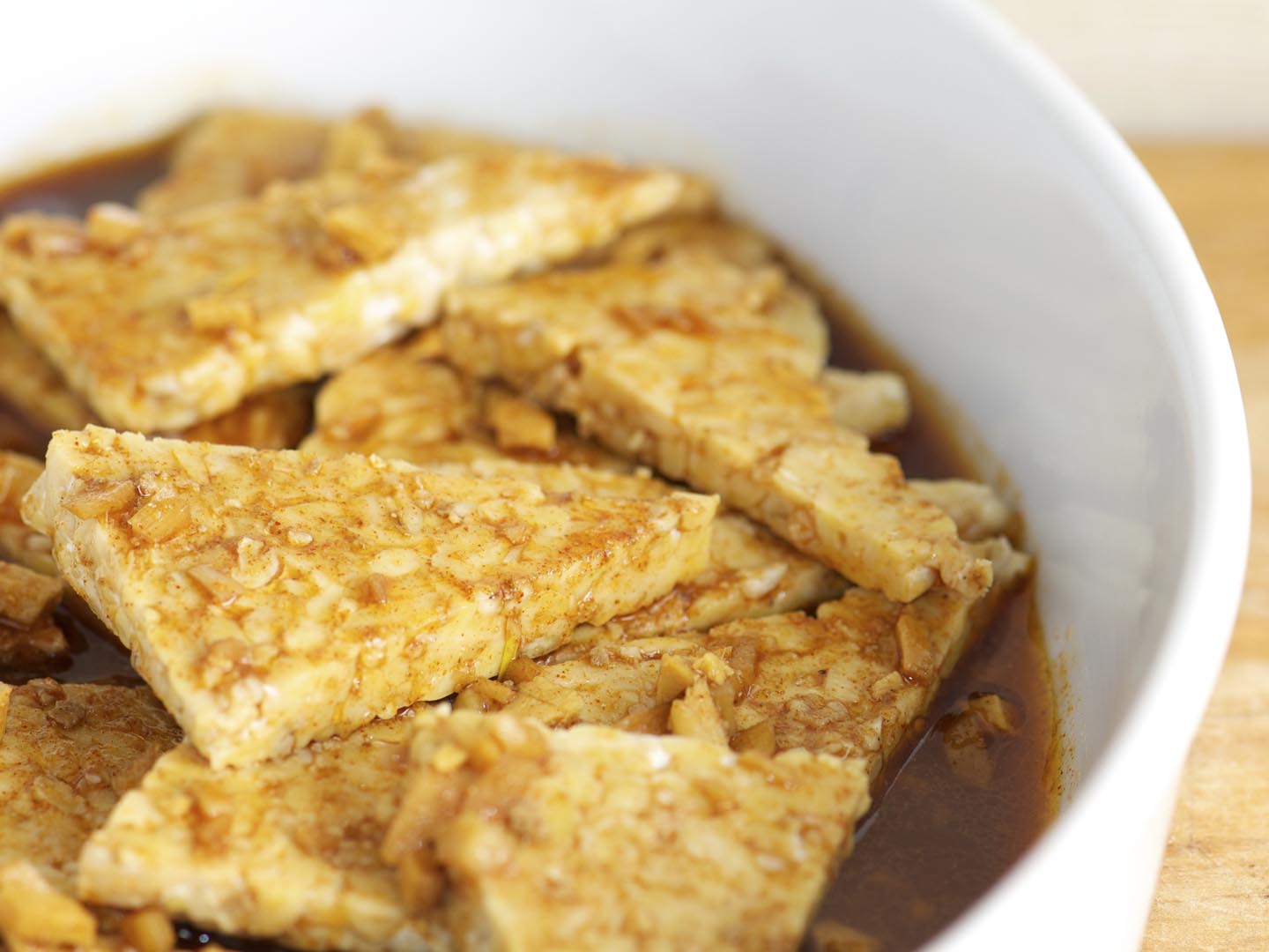 "Pieces of tempeh marinating in garlic, ginger, oil and spices in a white baking dish"