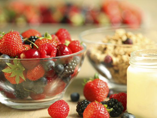 Healthy breakfast meal including a small jar of home made yoghurt, a bowl of granola and a variety of fresh summer berry fruit such as strawberry, blueberry, raspberry, blackberry, and cherry.