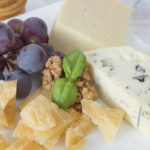 Different varieties of cheese, walnuts, red grapes and basil leaves