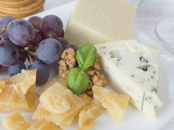 Different varieties of cheese, walnuts, red grapes and basil leaves