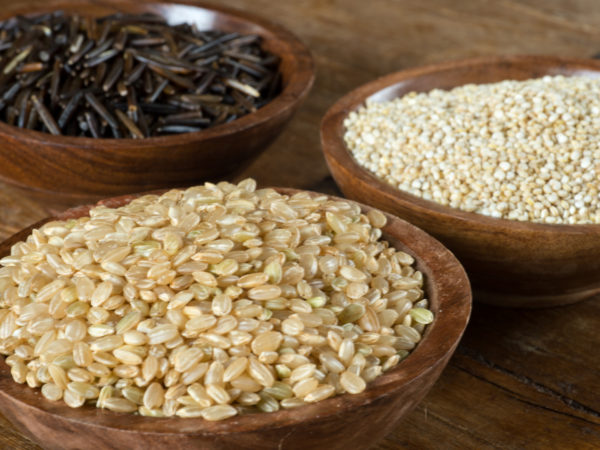 Small wood bowls filled with brown rice, quinoa and wild rice. This is shot on a wood table.