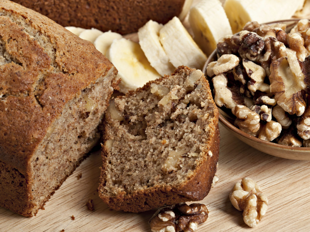 Sliced fresh baked banana bread with ingredients to bake it including walnuts and sliced fresh raw sweet bananas