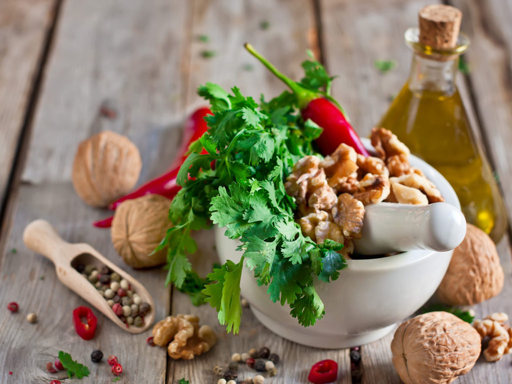 Cilantro, walnuts and red hot pepper in white ceramic mortar on wooden table