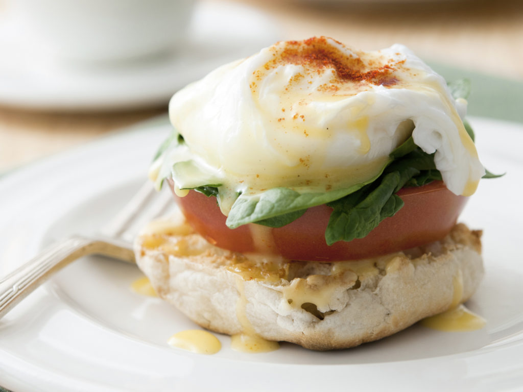 Closeup of vegetarian eggs benedict (eggs florentine) with fresh tomato and spinach. Selective focus; shallow depth of field.