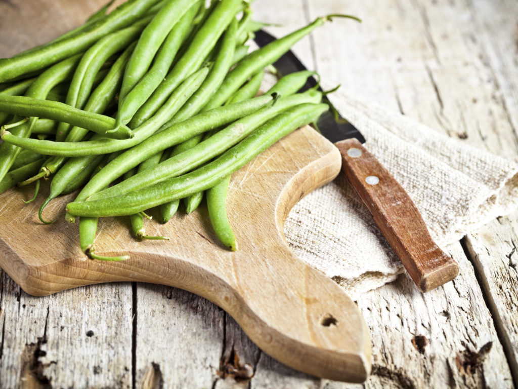 green string beans and knife closeup on wooden board