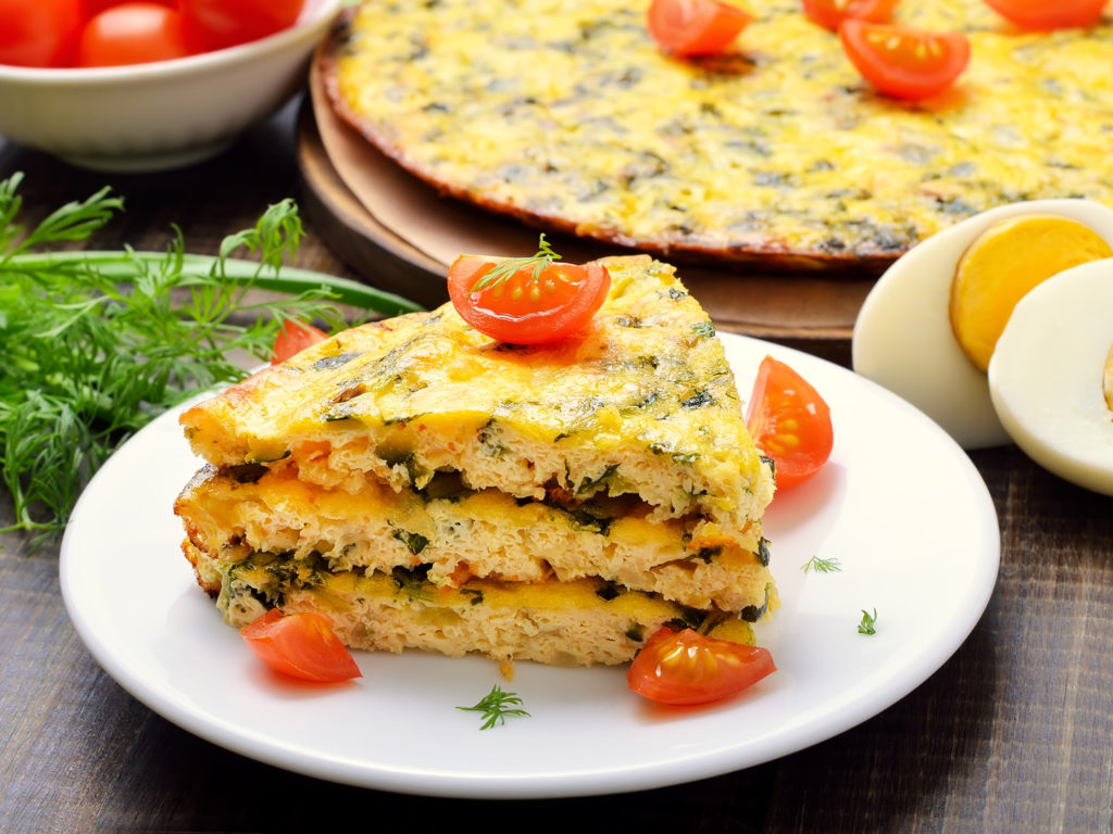 Homemade omelet with herbs and vegetables on wooden background, close up
