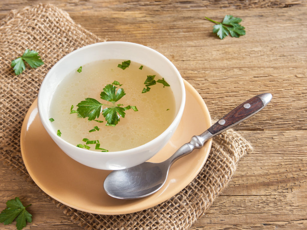 Chicken broth with parsley in white bowl over wooden background with copy space