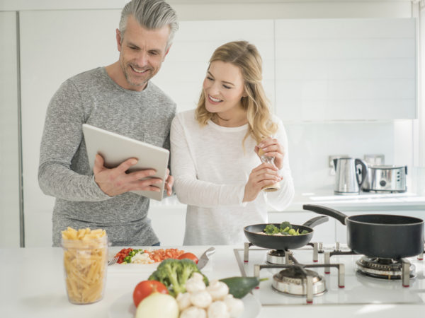 Couple cooking together at home following a recipe online on a tablet computer