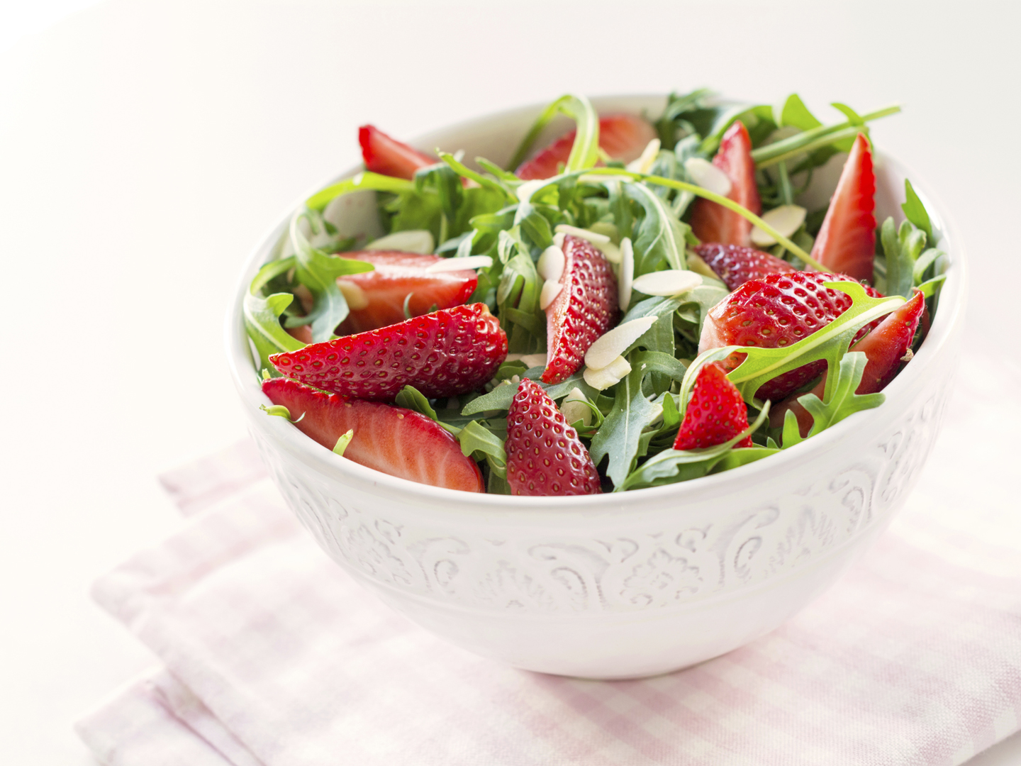 Healthy organic diet salad with arugula, strawberries, swiss chard and almonds in white bowl on pink napkin