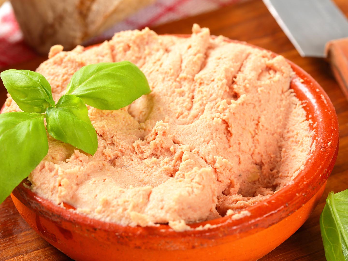 fresh liver pate with basil in orange ceramic bowl on a wooden cutting board
