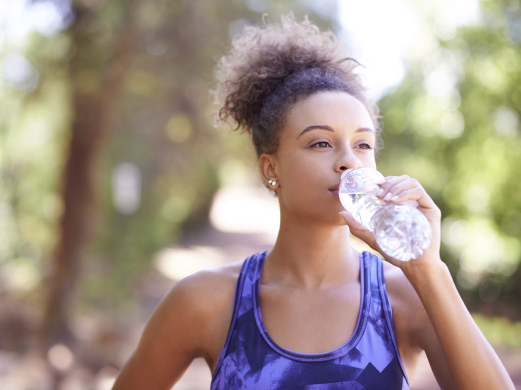 Shot of a sporty young woman drinking water after her workout
