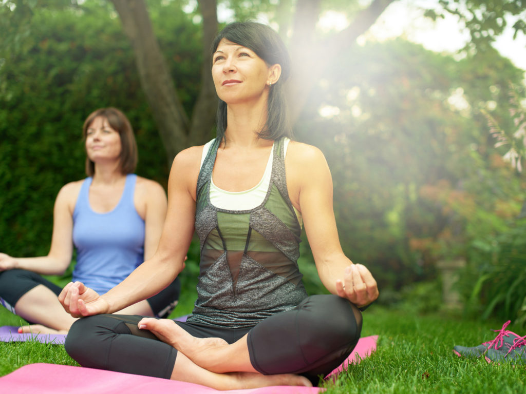 Couple of female friends in their forties connecting and staying healthy by practicing yoga i