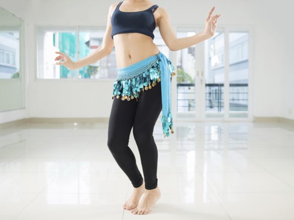 Belly dancer in legging and hip scarf dancing in the class