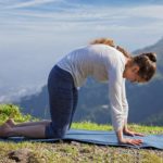 Yoga exercise outdoors - sporty fit woman practices yoga asana Marjariasana - cat pose outdoors in Himalayas