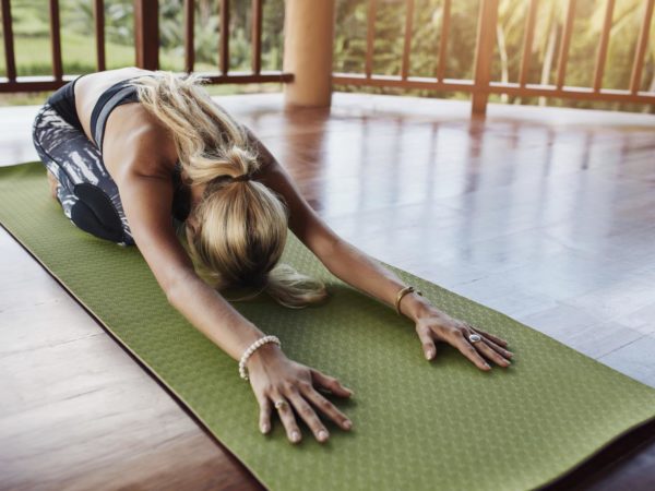 Young woman doing stretching workout on fitness mat. Female performing yoga on exercise mat at gym. Child Pose, Balasana.