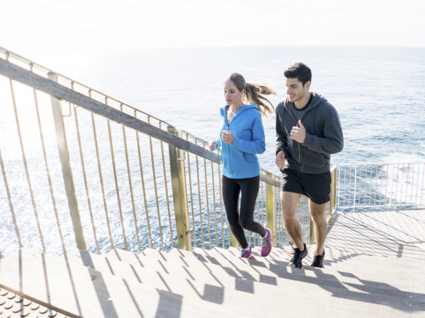 Happy couple running together outdoors climbing some stairs by the sea