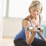 Fit mature woman lifting dumbbell while sitting at home