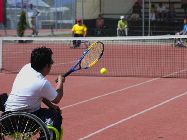 A wheelchair tennis player during a tennis championship match, taking a shot.