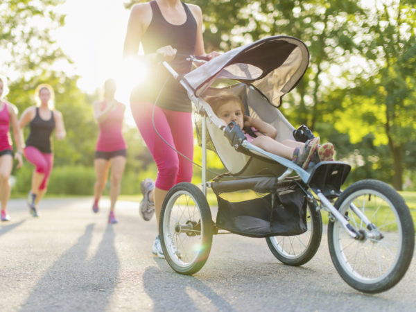 Woman pushing her toddler while running in nature with friends
