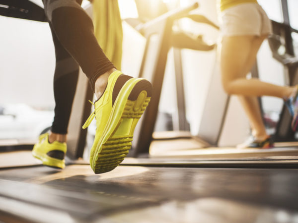 Two unrecognizable people exercising on treadmill in a health club.