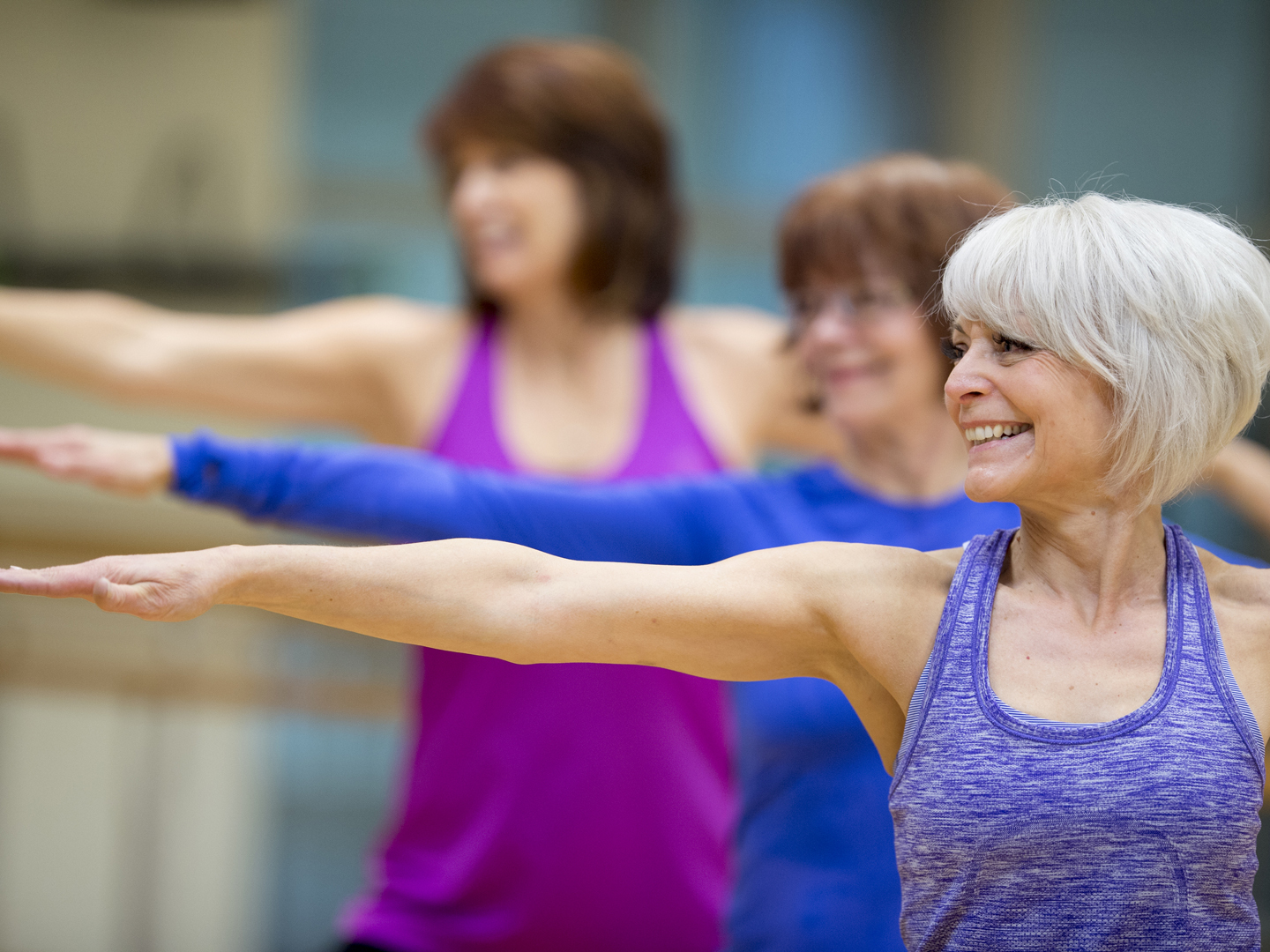 A group of senior adult women are taking a yoga class together at the gym.