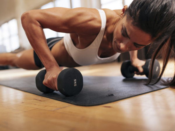 Strong young woman doing push ups exercise with dumbbells. Fitness model doing intense training in the gym.