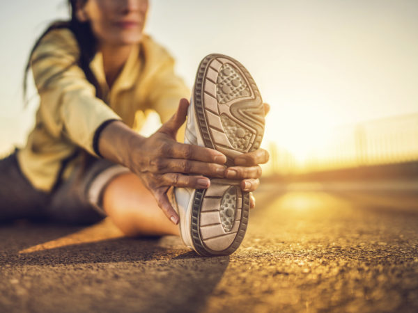 Close-up of athlete&#039;s sports shoe during stretching exercises on a road at sunset.