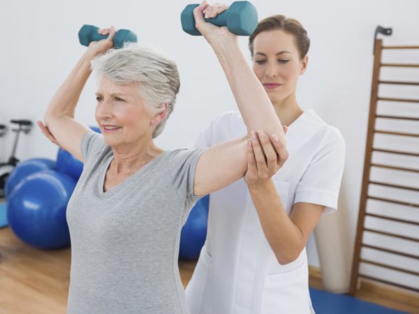 Female trainer assisting senior woman lifting weights in gym