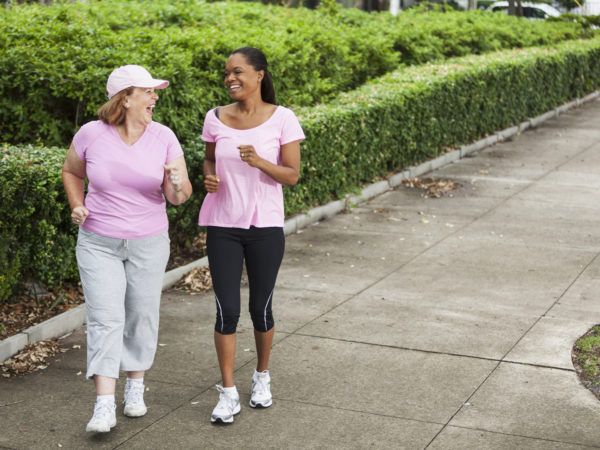 Senior woman (60s) with friend (40s) power walking together.
