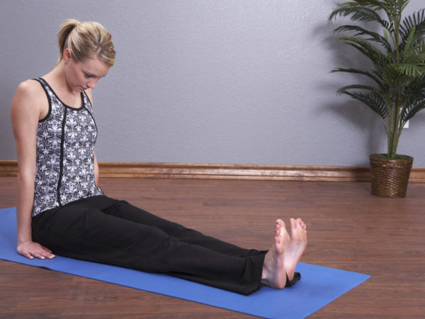 A young woman works out in yoga class. She is sitting in the staff pose - dandasana.