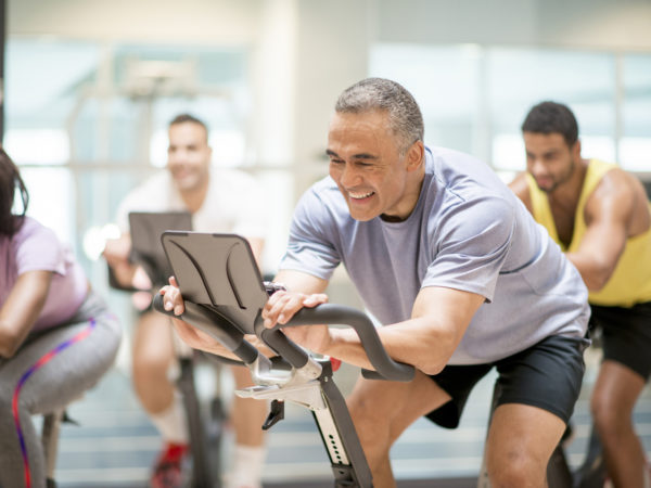 A multi-ethnic group of adults are taking a spin class together at the gym. They are working by cycling on stationary bikes.