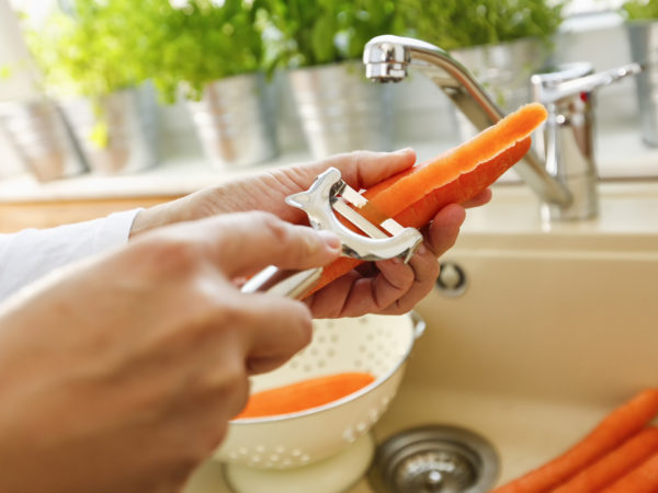 Peeling fresh carrots for preparing a healthy meal. You can use a peeler and peel the carrots over the sink. It is time saving and the carrots can be washed immediately.