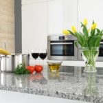 Tomatoes, herbs, wine and flowers on a granite counter top.